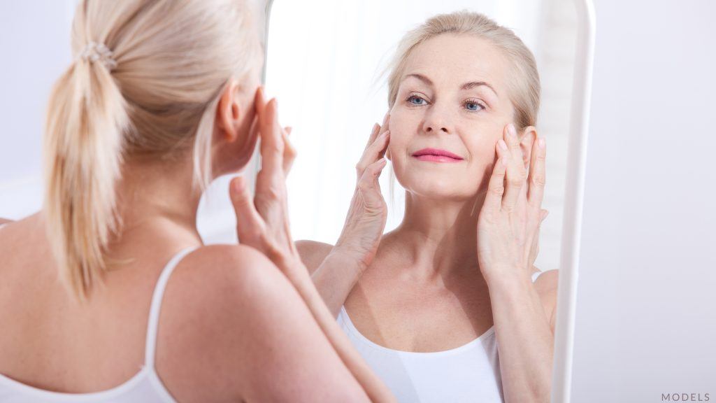 Older woman smiling and touching her face in the mirror (model)