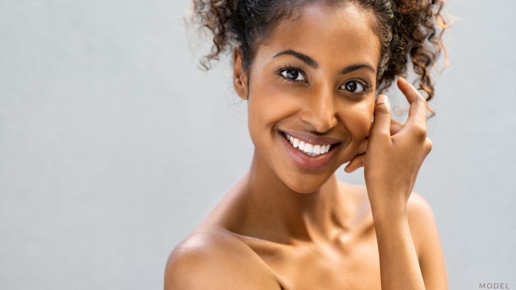 Woman with radiant skin smiling and touching her cheek (model)